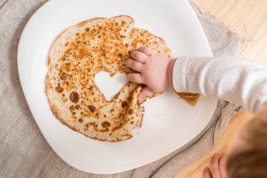 Bir kalp şeklinde krep yığını. Sevgililer günü kavramı ve tatil Maslenitsa üst görüntüleyin. Düz yatıyordu kopya alanı. Küçük çocukların elleri. Meraklı şirin bebek