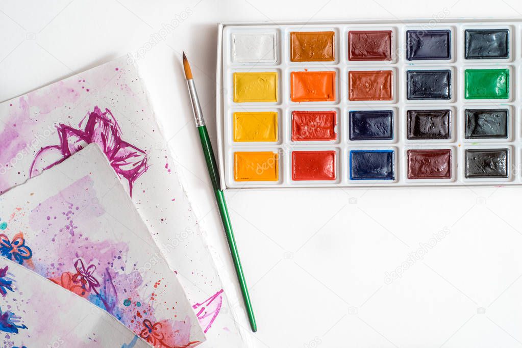 Watercolor paints, white sheet of paper and brushes View from above. Colorful paint. Creative artistic mockup with copyspace