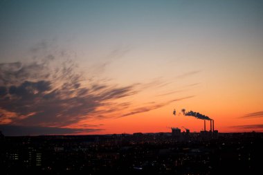 Renkli Sihirli Günbatımı. Gün doğumunda şehir evlerinin çatıları. Termik santral borusundan siyah duman geliyor.