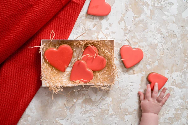 Homemade gingerbread with letters love for Valentine's Day on a background, Red icing, valentine hearts, top view. copy space. baby's hand, little baby