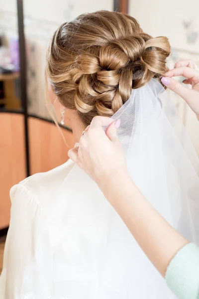 Blonde bride hairstyle. white veil. stylist helps the bride at home