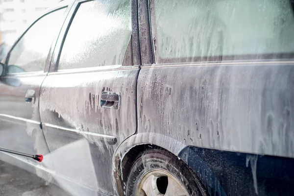 car wash, plenty of water and foam. drops drip down the windows of the car.