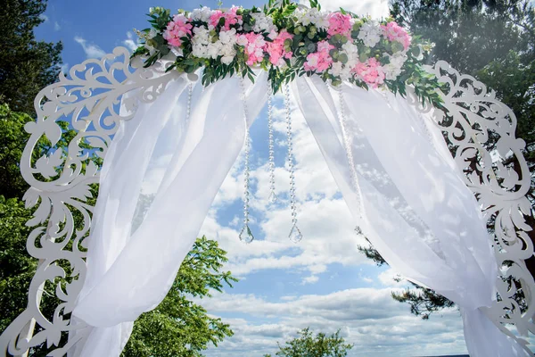 Weißer Bogen mit weißen und rosa Blumen im Freien. Festliches Dekor für die Hochzeit.Hochzeitshintergrund.Ort der Trauung im Freien. — Stockfoto