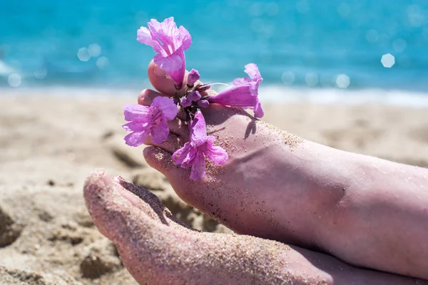 Bosé nohy na pláži, žlutý písek, exotická květina na nohou, horké slunce, modré moře. Léto a prázdniny — Stock fotografie