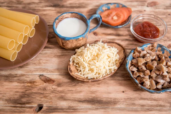 Concetto di cibo italiano. Ingredienti per la cottura della pasta. Pasta secca cannelloni, pomodorini, basilico fresco, aglio su fondo nero . — Foto Stock