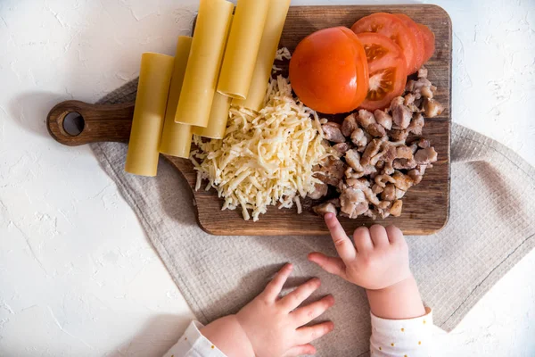 V kuchyni kuchař vaří špagety. vaří těstoviny Cannelloni. syrové těstoviny a bechamelová omáčka na bílém podkladu. Dětská ruka vzít těstoviny — Stock fotografie