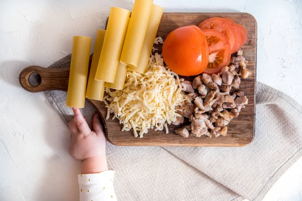 Chef cocinando espaguetis en la cocina. cocinar canelones de pasta. pasta cruda y salsa bechamel sobre un fondo blanco. manos de bebé tomar pasta — Foto de Stock