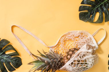 Pastel pembe tuval üzerinde limonlu ve ananaslı ağ alışveriş torbası..