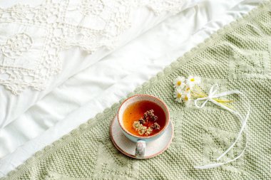 Yatakta naneli ve limonlu çaydan bir fincan doğal bitki çayı. Sıcak atmosfer. Çapraz dantel, pamuk beyazı battaniye, papatya çiçekleri. Kahvaltı..