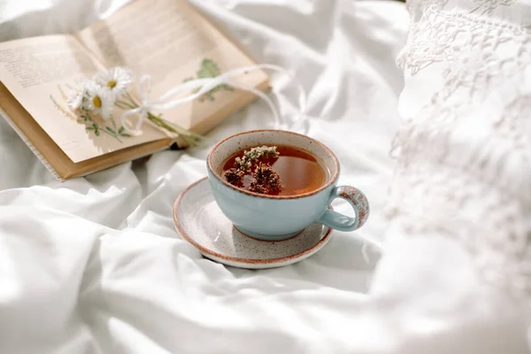 Šálek kávy a otevřenou knihu na bílém otevřeném lůžku. Ranní snídaně. Světlý útulný den — Stock fotografie