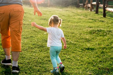 Bir ebeveyn küçük bir çocuğun elini tutar. Küçük kız gün batımında babasıyla el ele gider. güneşli bir akşam.