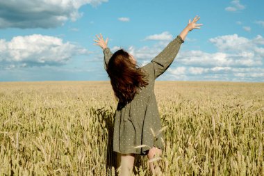 Genç kız buğday tarlasında dans ediyor. Elini kulaklarının üzerinden geçiriyor. Sırtını kolluyor. Rüzgarda uçuşan saçlar, yaşam tarzı. Duygusal olarak dönüyor ve zıplıyor. özgürlük kavramı ve sıcak yaz.