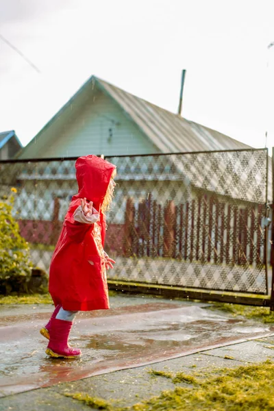 赤いジャケットのかわいい女の子が水たまりに飛び込んでいます暖かい夏や秋の太陽を設定します 村の夏 — ストック写真