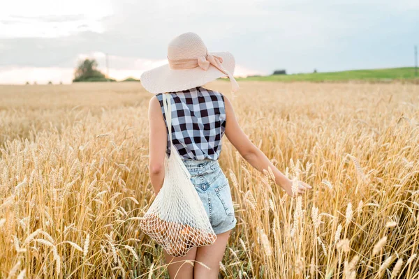 Sırtında altın buğdayla gezen mutlu kız, açık hava yaşam tarzıyla. Özgürlük kavramı. Yaz tarlasında tatlı küçük bir kız. Ekmek torbasından ekmek alıp, elinde ip torbası tutuyor..
