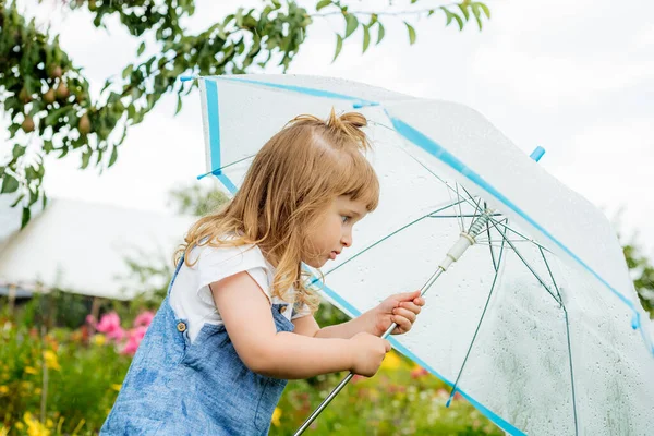 Little girl with umbrella playing in the rain. Autumn outdoor fun for children. Toddler kid outside in the garden. Baby enjoying summer shower