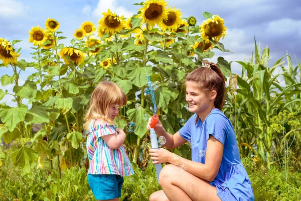 Two smiling happy children in sunflowers field laugh and blow bubbles. summer in the village. — Stock Photo, Image