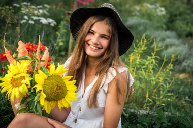 Köydeki şirin küçük kız çiftçi. Sarı ayçiçeği ve sebze hasadı, ellerinde sonbahar buketi. Açık havada.