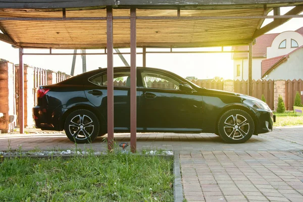 The car is under a canopy, an open garage, the territory of the will of the house