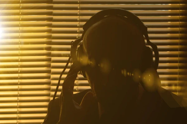 秘密のエージェントは ブラインド 太陽のまぶしさとトーンで窓の背景にヘッドフォンで会話を聞きます — ストック写真