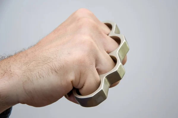 Man strikes brass knuckles on a light background, a prohibited weapon in a fight