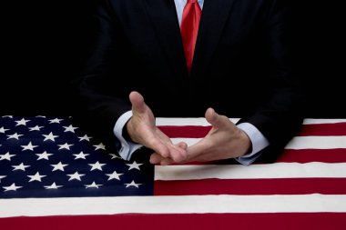 Bir Amerikan bayrağı ile kaplı bir masada, bir erkek işadamı ve politikacı diyalog ve öneriler için ellerini dışarı tutar, ortalama plan