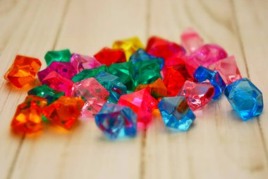 Ahşap bir masaya saçılmış renkli taşlar, hareket kabiliyeti geliştirmek için çocuk oyuncakları, plastik mücevherler..