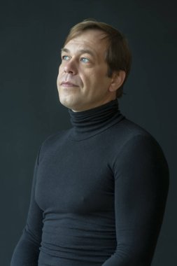 Dar siyah elbiseli çok ciddi bir adam ışığa bakıyor. Yetişkin erkek, 40 yaşında.+