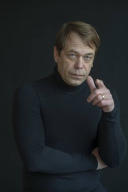 Siyah elbiseli çok ciddi bir adam parmaklarını bir şeye doğrultuyor. Yetişkin erkek, 40 yaşında.+