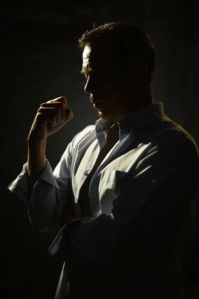 Portrait of a thoughtful 45-50-year-old man in a blue unbuttoned shirt of athletic build, contour lighting, dark background.Maybe he's a former athlete, a retired military man, a truck driver,