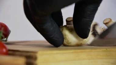 Siyah eldivenli bir şef pizzacıda mantar doğruyor. Tahtada metal bir bıçakla, ağır çekimde, hafif mutfakta, yakın çekimde..