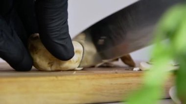 Siyah eldivenli şef pizzacıda mantarları ince ince doğruyor tahta bir tahtanın üzerinde metal bir bıçakla, yavaş çekimde, parlak mutfakta, yakın planda..