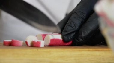 Mutfaktaki aşçı bıçakla yengeç çubuklarını ince ince doğruyor. Yemek hazırlama ve yemek pişirme.