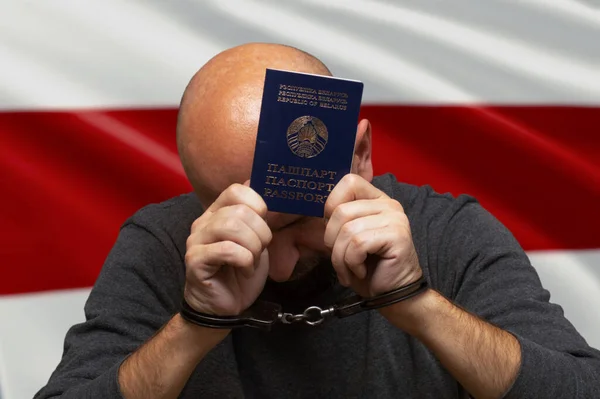ベラルーシの白赤白国旗を背景に手錠をかけられた男がパスポートを手に持っている 違法防衛と逮捕 デモ参加者の裁判 野党の政治的抑圧 — ストック写真