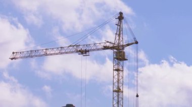 Yüksek katlı bir vinç mavi gökyüzü ve bulutların arka planına karşı dönüyor..