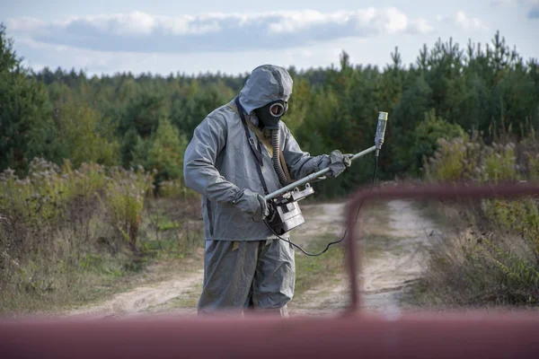Ein Militärmann in einem Chemikalienschutzanzug misst die Strahlung mit einem Dosimeter, das vor einer Absperrung steht — Stockbild Ein Militärmann Einem Chemikalienschutzanzug Misst Die Strahlung Mit Einem Dosimeter — Stockfoto