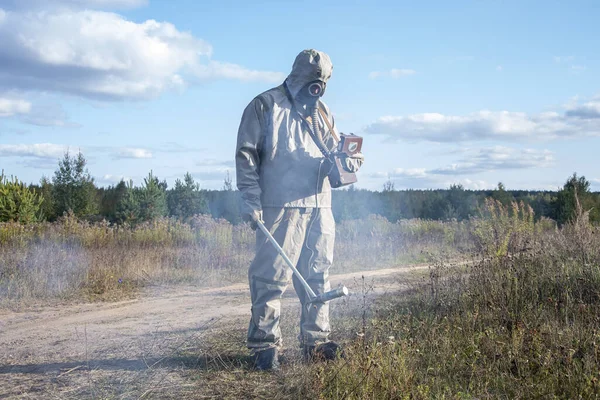 Ein Soldat in einem Chemikalienschutzanzug überprüft das radioaktive Gebiet mit einem Dosimeter vor dem Hintergrund wilder Vegetation und des Himmels mit Wolken. Rauch schädlicher Dämpfe breitet sich aus. — Stockbild Ein Soldat Einem Chemikalienschutzanzug Überprüft Das Radioaktive Gebiet Mit Einem — Stockfoto