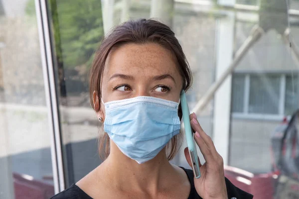 Street portrait of a woman in a medical mask talking on the phone, close-up, selective focus.