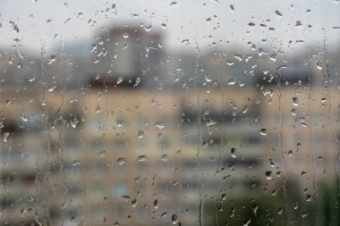 Pencerede yağmur damlaları, bulanık şehir manzarası, seçici odak.