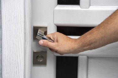 Yaşlı bir adamın eli beyaz bir kapıyı modern bir tasarımın kapı koluna basarak açar. Yakın plan, seçici odaklanma. Konsept: Yeni bir dairede yenileme, emekliler için modern mobilya.