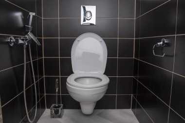 Ev tuvaleti, siyah kiremitlerle kaplı duvarlar, açık kapaklı bidet ve tuvalet, modern iç tasarım, tesisat.