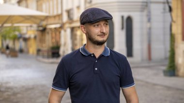 30-35 yaşlarında sakallı bir gencin sokak portresi eski şehrin tarafsız arka planına bakıyor.,