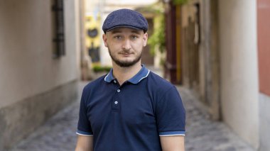 30-35 yaşlarında, sakallı, ciddi bir gencin sokak portresi. Eski şehrin arka planında kameraya bakıyor.,