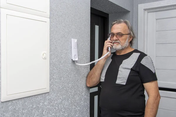 Portrait of an elderly man 60-65 years old talking in an apartment on the intercom. Concept: security and a sense of stability and the absence of anxiety for their own lives.