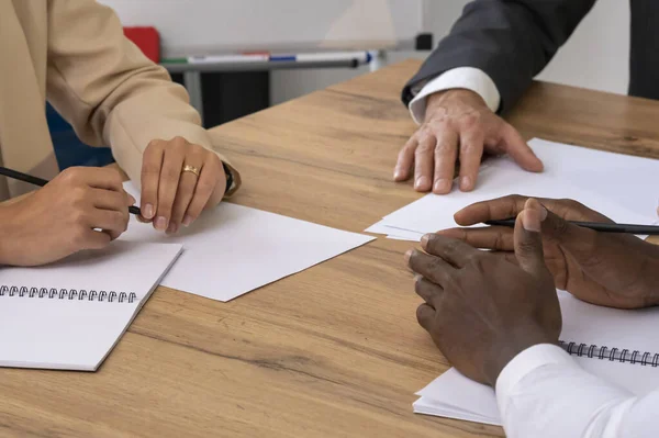 The hands of a black man, a white woman, and a white man lie on the table, close-up, selectively focused.  Concept: business meeting of business partners in the conference hall.