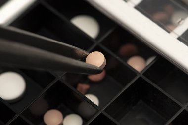 Tablet günlük tıbbi organizatörden alınan cımbızla alınıyor, yakın plan, seçici odaklanma. Konsept: evde tedavi, zamanında ilaç almak.