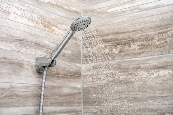 From the shower mounted on the wall, water flows into the bathroom, close-up. Modern interior and interior decoration.