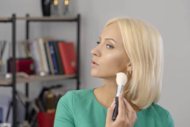 25-30 yaşlarındaki genç sarışın kadın yüzüne makyaj yapıyor..