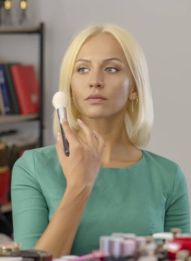 25-30 yaşlarındaki genç sarışın kadın yüzüne makyaj yapıyor..