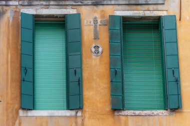 Süslü haçlı sarı bir duvarda yeşil panjurlar.