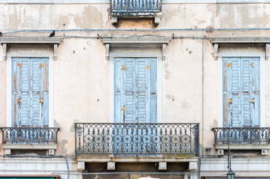 Evin balkonları ve pencerelerinde mavi panjurlar, işlenmiş demir korkuluklar ve soyulan alçılarla doludur.